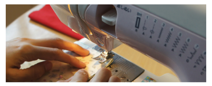 Close up image of hand guiding material through a sewing machine